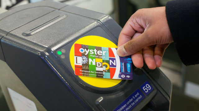 Vous pouvez acheter une carte Oyster pour visiteurs avant votre arrivée à Londres. Image reproduite avec l'aimable autorisation de Shutterstock. Gros plan d'une carte Oyster Visiteur des transports londoniens avec un lecteur de carte Oyster jaune en arrière-plan.