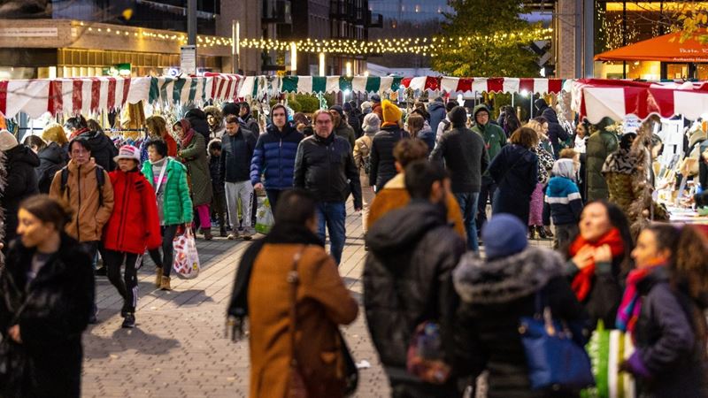 Pick up stocking fillers at Wembley Park Christmas market and admire the twinkling lights adorning the area. Credit: Amanda Rose. Image courtesy of Wembley Park. A photo of people walking around Wembley Park Christmas market with stalls and Christmas lights dotted around the area