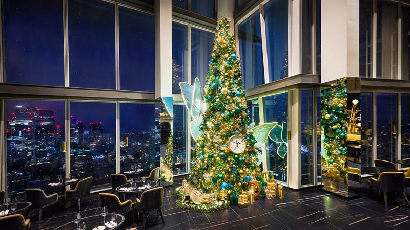 See the Peter Pan-themed tree add a festive twinkle to Aqua Shard across Christmas. Credit: Ben Carpenter. Image courtesy of Aqua Shard. A photo of the Christmas tree in the corner of Aqua Shard with fairy wings and colourful lights and baubles in green hues with a clock decoration in reference to Peter Pan