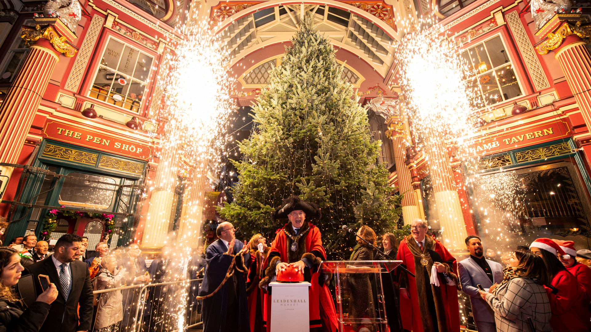 Head to the famous Victorian market decorated for the festive season along with its Christmas tree. Credit: Lucy Young. Image corutesy of Leadenhall Market. The Lord Mayor of London pushing a large red button as lights switch on the large Christmas tree inside Leadenhall Market, surrounded by crowds of people