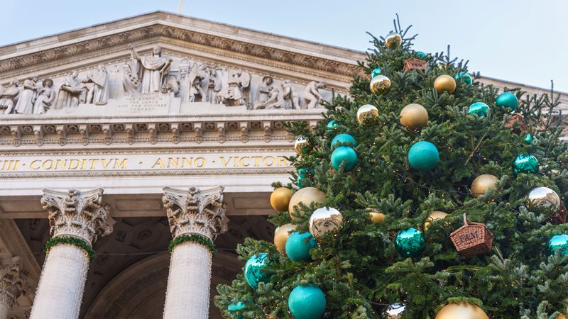 Visit the Fortnum & Mason Christmas tree outside The Royal Exchange. Credit: Philip Meech. Image courtesy of The Royal Exchange. A photo of the Christmas tree in front of the Royal Exchange with blue and gold Fortnum and Mason baubles and twinkling lights around the building's columns