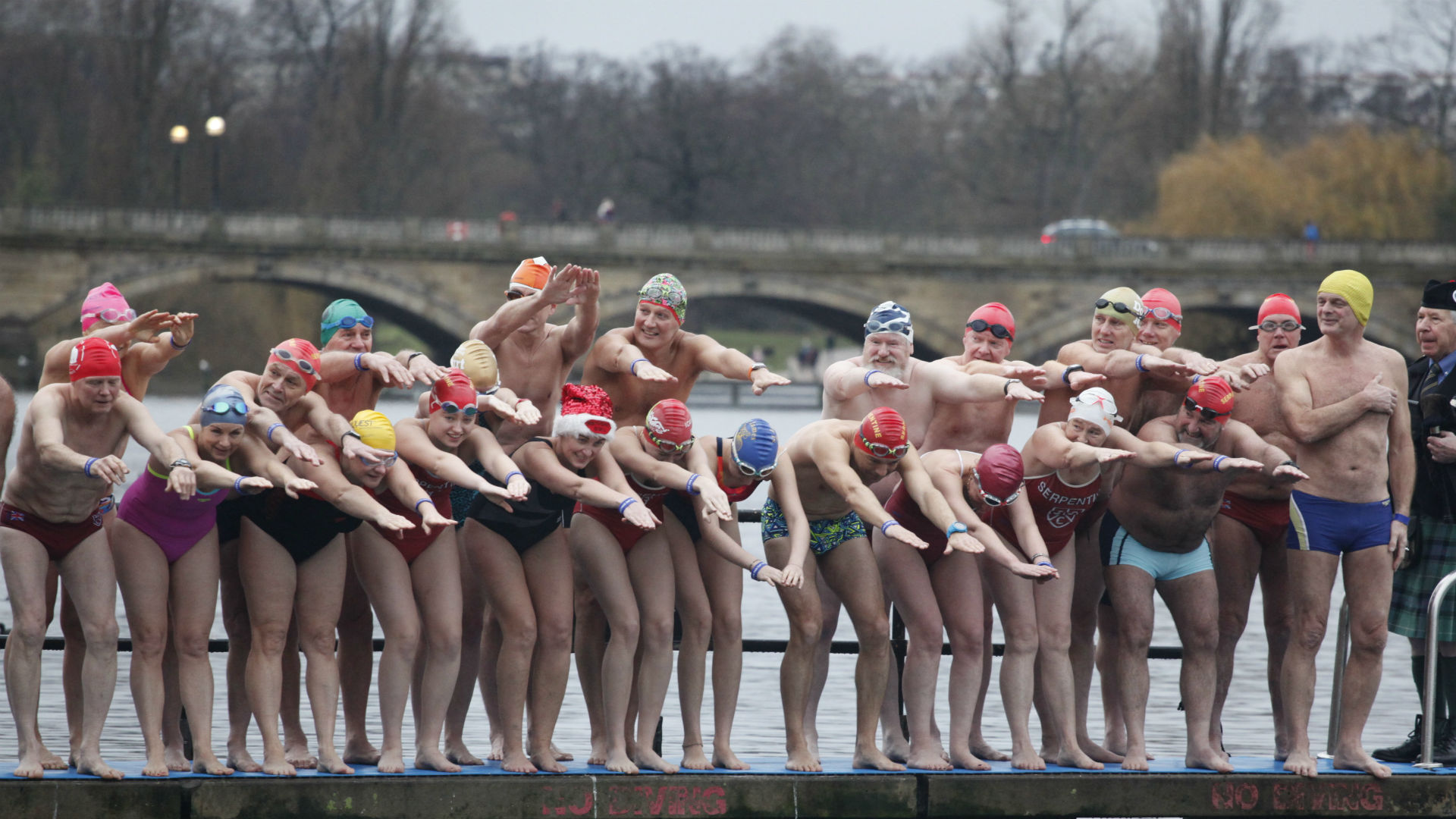 The Christmas Day Peter Pan Cup at the Serpentine in Hyde Park. Image courtesy of Serpentine Swimming Club. People in their swimming costumes about to jump into the water during The Christmas Day Peter Pan Cup in Hyde Park.