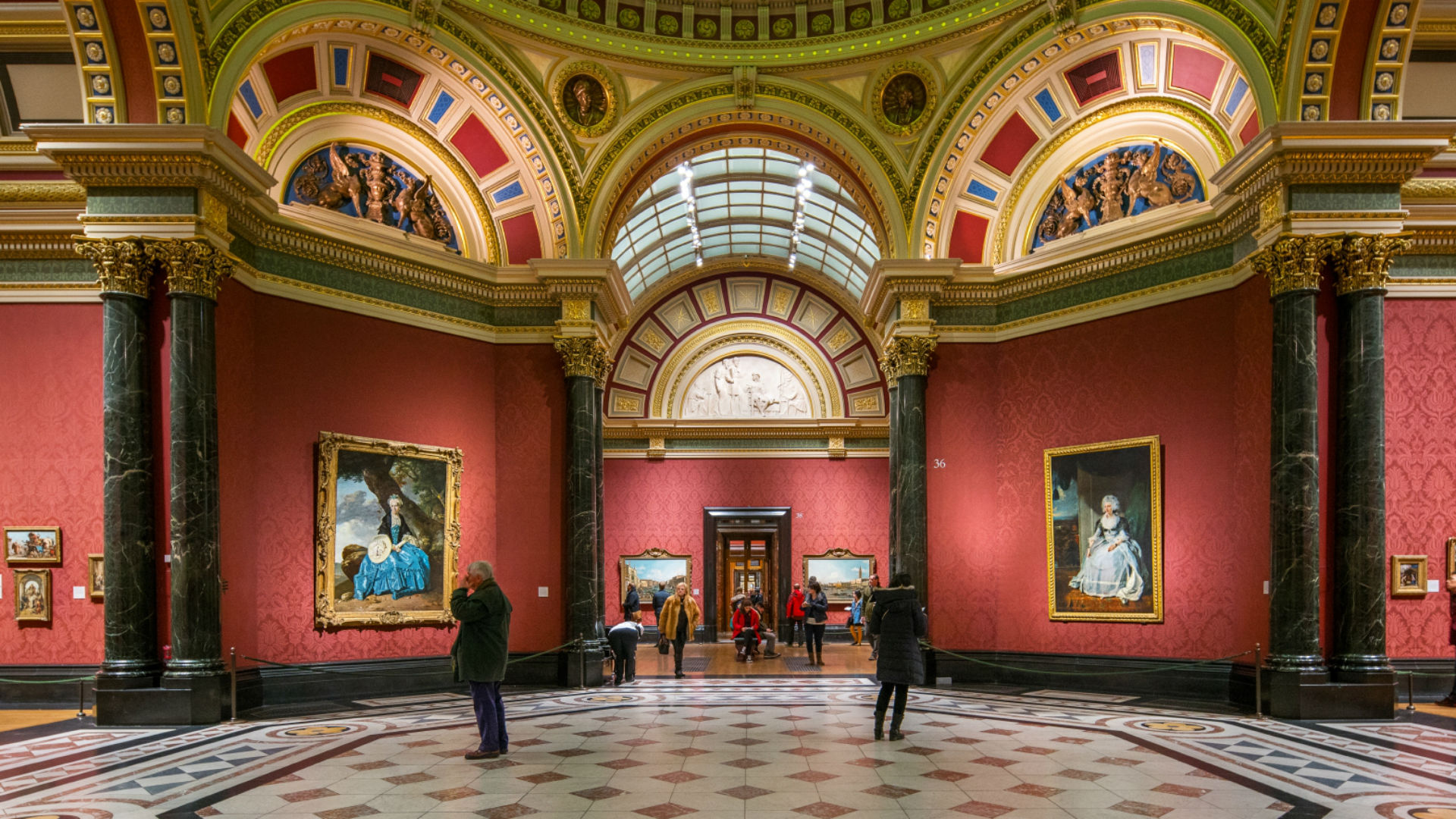 Explore London's National Gallery on a guided tour. Image courtesy of the National Gallery. Two people looking at paintings in the red-painted halls of the National Gallery.