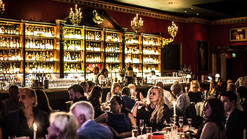 Pair groovy music with food and whisky bars at Boisdale Canary Wharf. Credit: Boisdale Canary Wharf. Image courtesy of Boisdale. Crowds sit at round tables with a backdrop of warm lighting at Boisdale Canary Wharf
