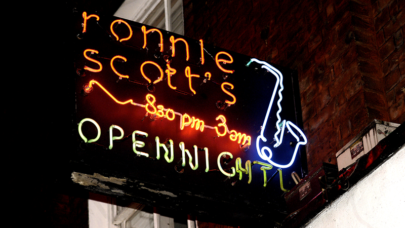 Find world-class acts play at the legendary Ronnie Scott's jazz club. Credit: Ronnie Scott's. Image courtesy of Ronnie Scott's. Neon sign to Ronnie Scott's jazz club which says "ronnie scott's 8.30pm-3am open nightly" with a trumpet