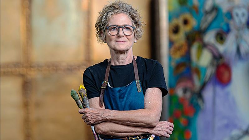 Spot works by local artists at Croydon Art On Our Doorstep, including Rachel Gadsden's community-led centrepiece. Image courtesy of Collective Wisdom. A portrait of artist Rachel Gadsden, holding paintbrushes, with an artwork in the background.