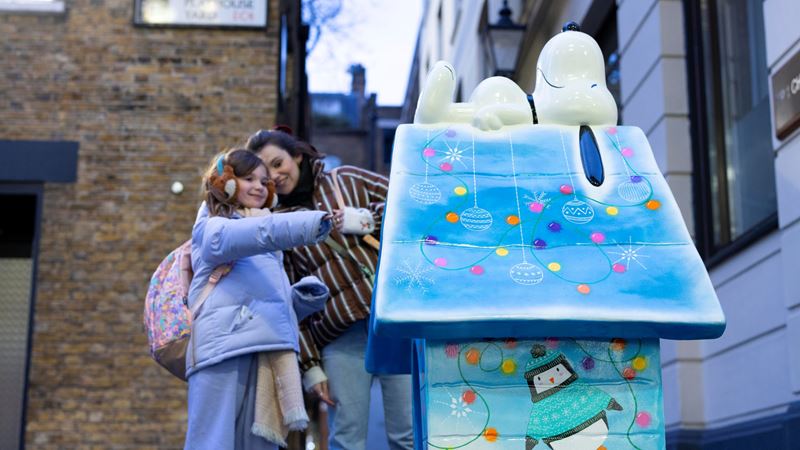 See how many Snoopy designs you can spot across Fleet Street Quarter this winter. Credit: David Parry/PA Media Assignments. Image courtesy of Fleet Street Quarter. A photo of a mother with a young girl dressed in a purple coat with gloves and earmuffs pointing at a sculpture of Snoopy sleeping on his kennel along the Fleet Street Quarter trail