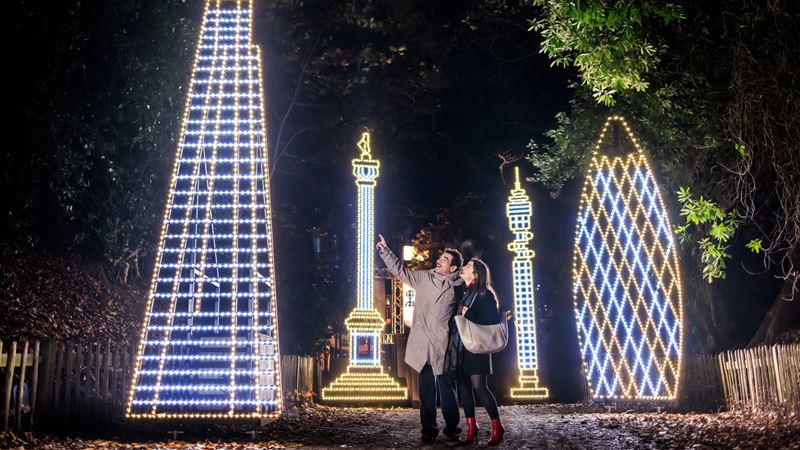 Wrap up and wander around Kenwood with its Peter Pan-themed lights this Christmas. Credit: Oliver Dixon. Image courtesy of Kenwood House. A photo of a man and woman pointing and looking up at a giant light installation of The Shard with other buildings in the background of London landmark inspired lights