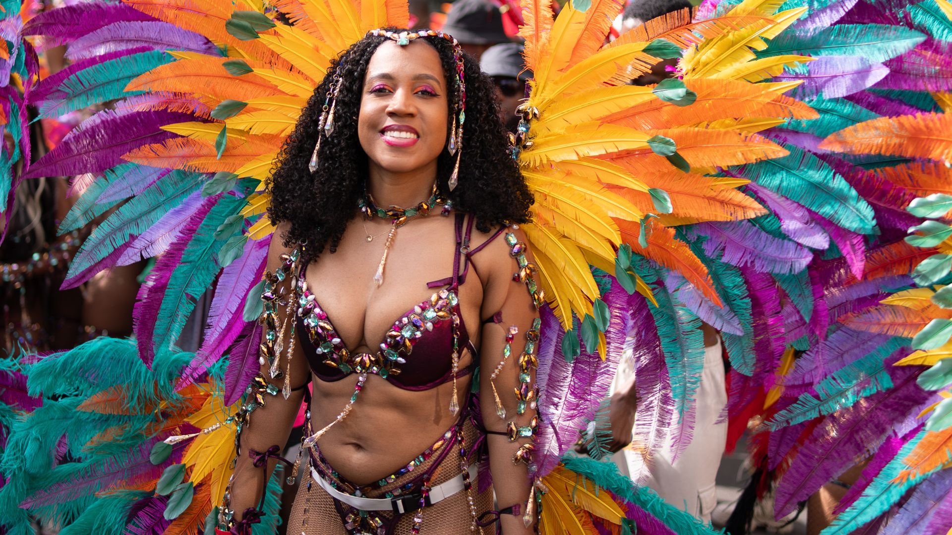 Admire the spectacular feathered costumes that bring the Notting Hill Carnival parade to life. Image credit: London & Partners/Peter Cohen. A carnival performer wears a vibrant costume with orange, yellow, purple and turquoise feathers at Notting Hill Carnival