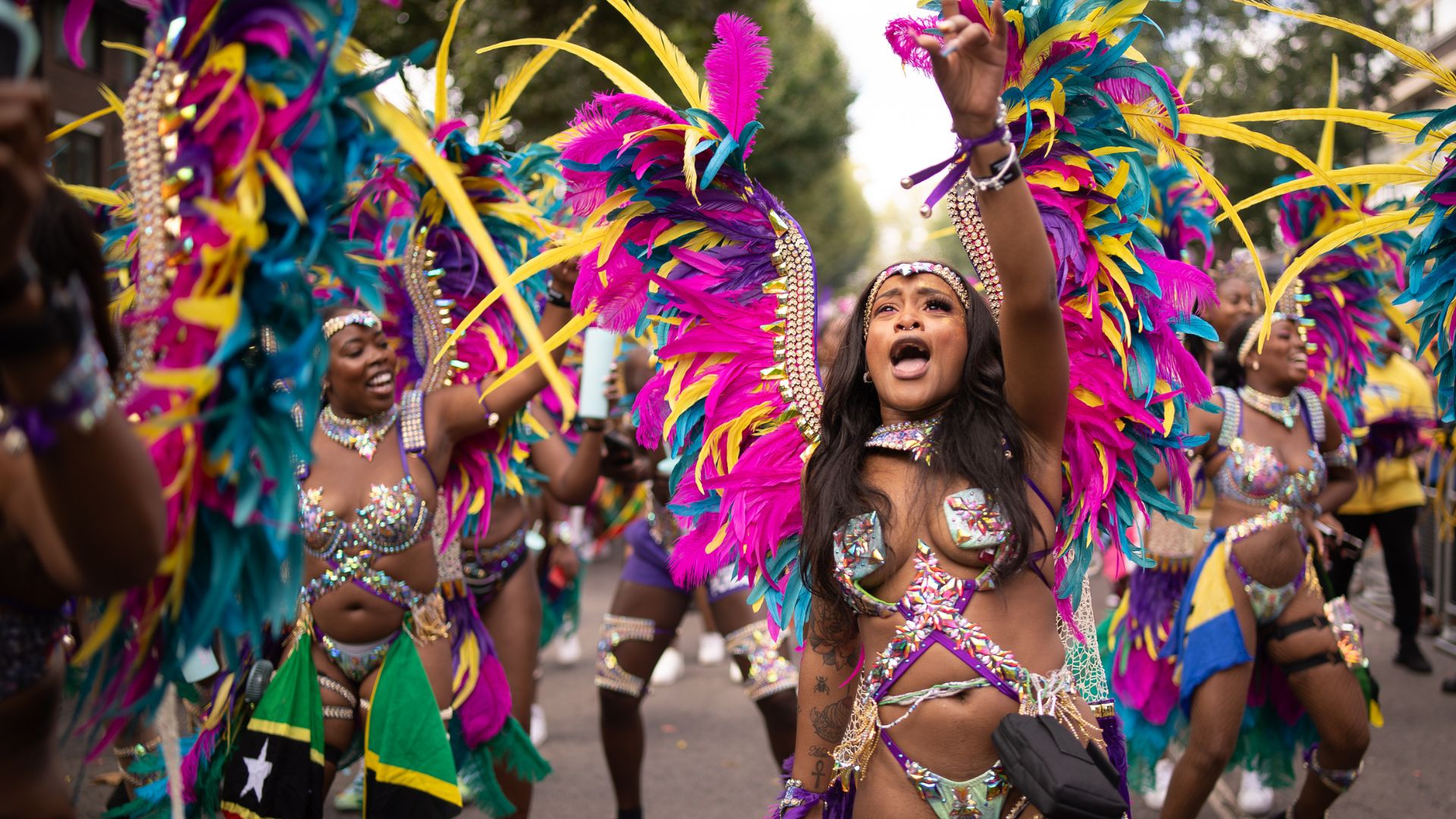 Join the celebrations as masquerade bands dance through the streets in dazzling feathered costumes.Image credit: London & Partners/Peter Cohen. Carnival dancers wearing colourful feathered costumes perform in the Notting Hill Carnival parade.