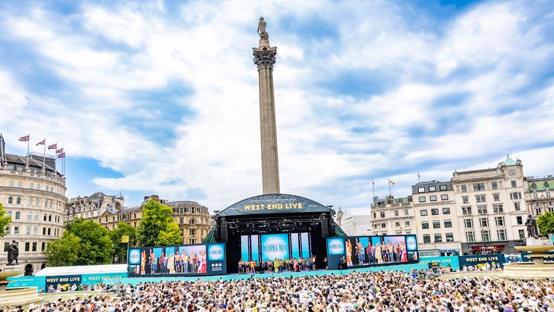 Mamma Mia! performance at West End Live 2025 © Danny Kaan. Image courtesy of Society of London Theatre. A crowd of people in Trafalgar Square look at the stage in front of Nelson's Column, during a performance from Mamma Mia! at West End Live.
