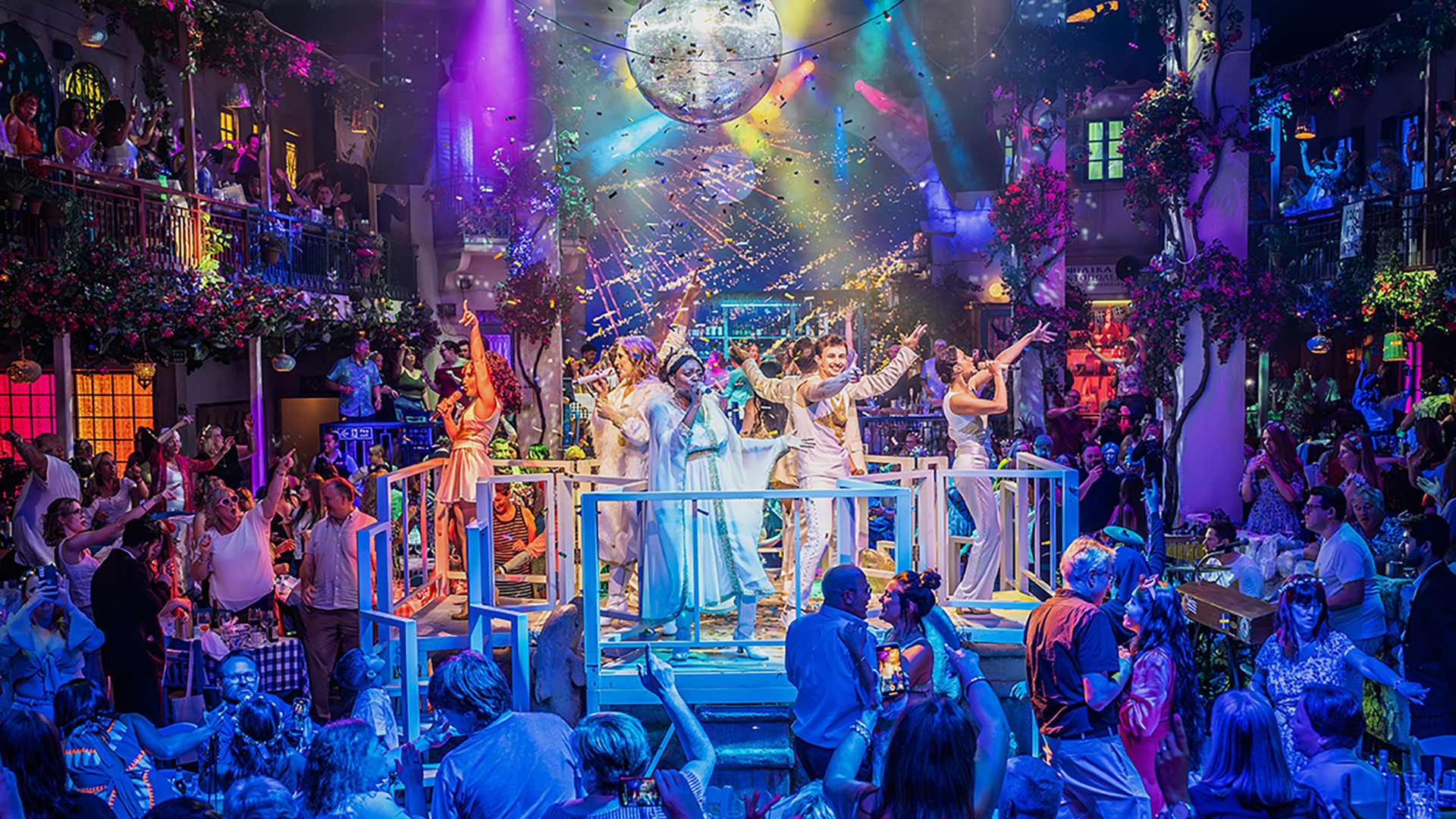 Take to the dance floor in true Dancing Queen style at the Mamma Mia! The Party, where guests gather to dance to ABBA's greatest hits after the show. Image courtesy of ABout Grace PR/ photo credit: Marc Brenner. Mamma Mia! The Party cast members, dressed in sparkly white outfits, sing and dance on a small elevated stage as members of the audience join in.
