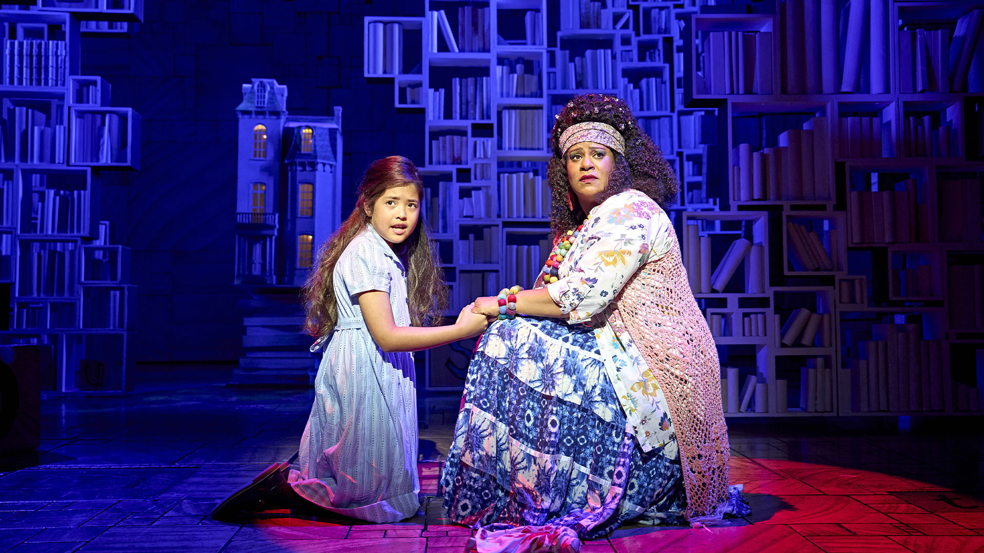 See the ever-popular Matilda The Musical and follow bookworm Matilda's journey from fighting for a place at home to navigating a new school. Image courtesy of London Theatre Direct/ Photo credit: Ellie Kurttz. Matilda and the librarian stands on the stage of the Cambridge Theatre holding hands and looking at the audience with a worried look.