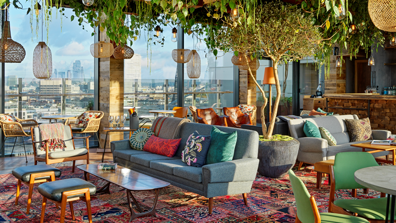 Marvel at the scenery at Madera at Treehouse London restaurant. Credit: Bacchus Agency. Image courtesy of Bacchus Agency. Trailing plants hang from the ceiling of the Nest lounge at Treehouse London with red Persian rugs, wooden hanging pendant lights and comfy chairs and sofas with floor-to-ceiling windows boasting a view of London's cityscape
