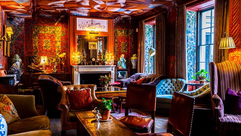 Warm up next to the fireplace at The Zetter Clerkenwell hotel. Credit: The PC Agency. Image courtesy of The PC Agency. Communal area at Zetter Townhouse Clerkenwell with red patterned wallpaper, velvet sofas and wooden tables